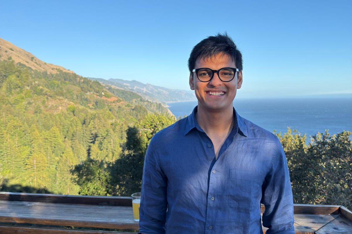 Shivam Raval standing at a wooden railing above a forested hillside and the ocean